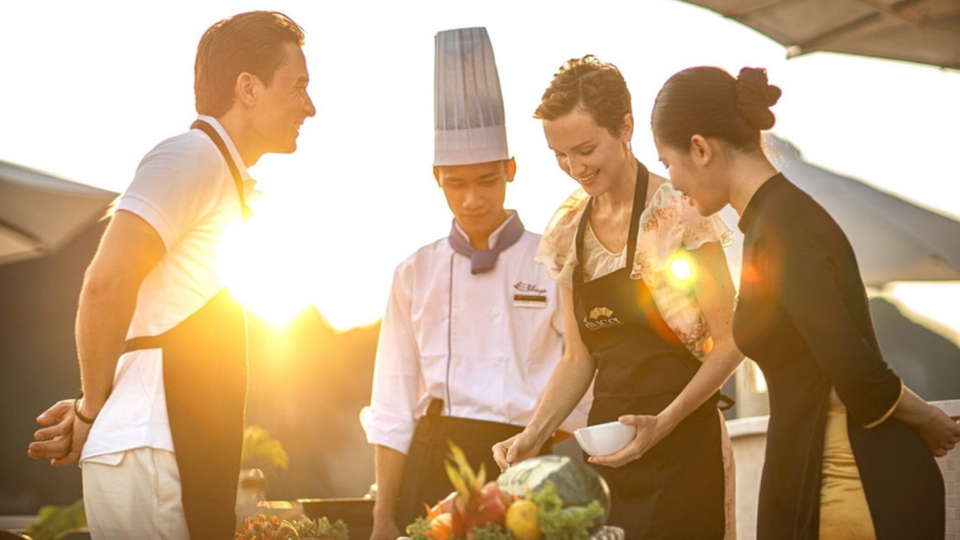 Travellers cooking on a Halong Bay junk boat cruise next to a chef and an attendant