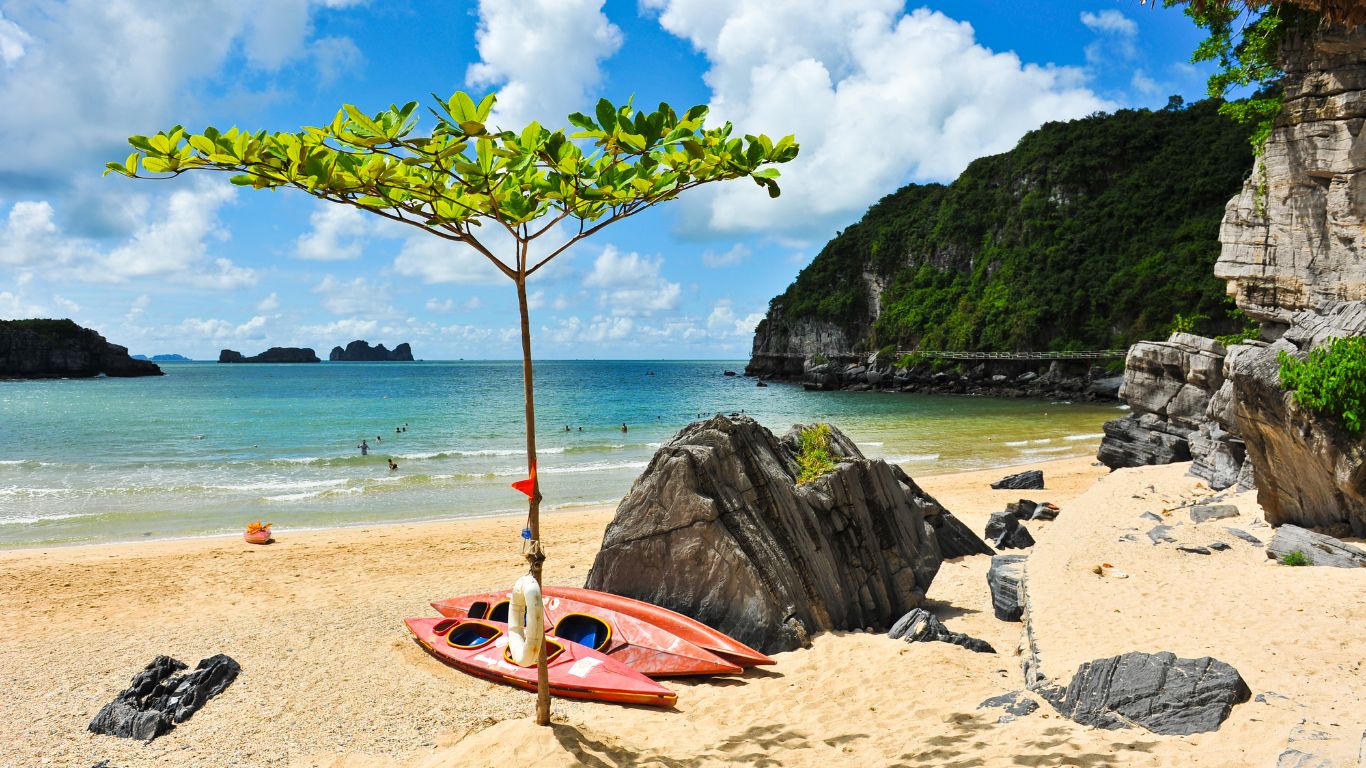 Cat Co beach Cat Ba Island with kayaks on golden sand turquoise water and limestone karst cliffs Vietnam