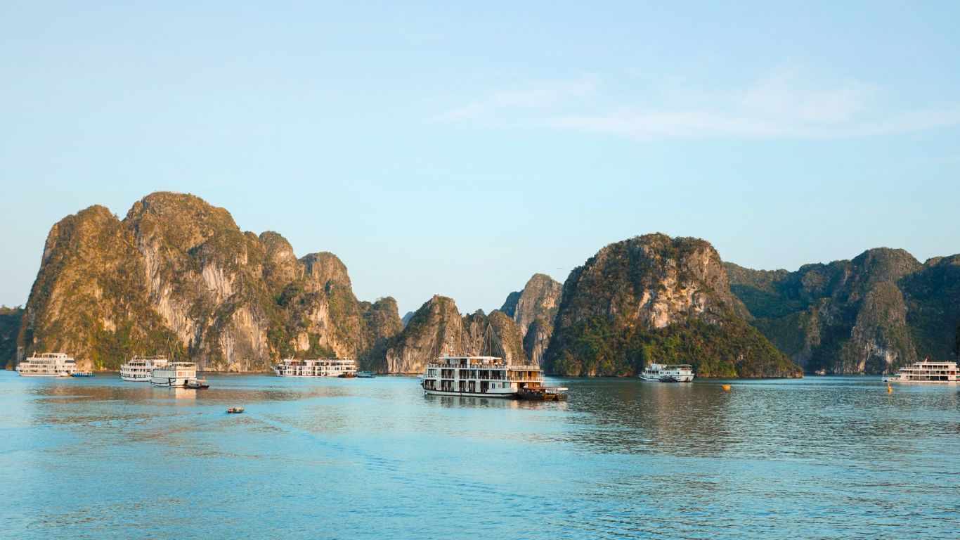 Cruise ships sailing through Halong Bay surrounded by towering limestone karsts on a sunny summer day in Vietnam.
